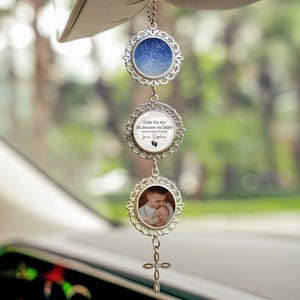 May include: A silver car charm with three circular pendants. The top pendant displays a blue night sky design. The middle pendant has text that reads "Under this sky You became my Daddy" and a baby footprint. The bottom pendant holds a photo of a man holding a baby.