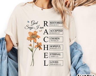 May include: Ivory-colored t-shirt with the text "God Says I am RACHEL" and floral graphics. The design includes the words "Restored, Accepted, Chosen, Hopeful, Eternal, Loved" with corresponding Bible verses.