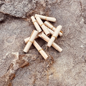 May include: A collection of small, rolled paper scrolls secured with gold-colored metal rings. The scrolls are a light tan color and are scattered on a rough, gray and brown stone surface.