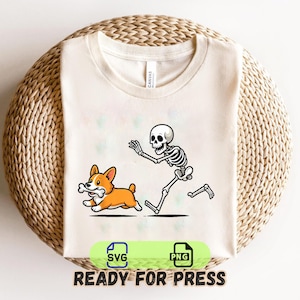 May include: A cream-coloured t-shirt featuring a graphic of a skeleton chasing a brown and white Corgi dog that is carrying a bone in its mouth. Below the graphic are two green icons labelled SVG and PNG, followed by the text READY FOR PRESS.