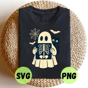 Puede incluir: Camiseta negra con un diseño temático de Halloween. Un fantasma sostiene una radiografía, con un gato negro, murciélagos y una telaraña. La camiseta tiene etiquetas SVG y PNG en círculos verdes.