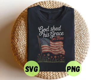 May include: A black t-shirt featuring a graphic print of an American flag on a flagpole with the text God shed his Grace on thee above it. Below the flag are small red flowers and green stems. The design has a distressed, vintage-style texture.