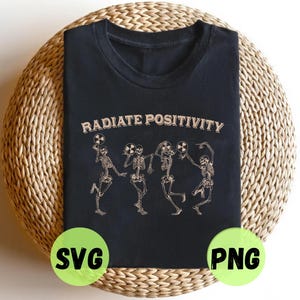 Könnte beinhalten: Schwarzes T-Shirt mit dem Schriftzug "RADIATE POSITIVITY" über einer Grafik von tanzenden Skeletten, die Atomsymbole halten. Das Shirt liegt auf einer gewebten, kreisförmigen Oberfläche. Grüne Kreise mit "SVG" und "PNG".