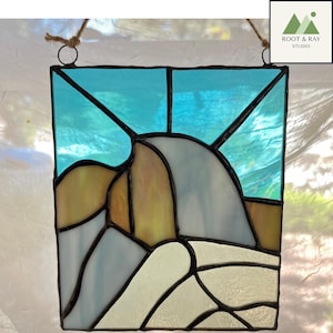 May include: Stained glass panel featuring a mountain landscape with a blue sky. The artwork uses shades of blue, yellow, and white, with black lines defining the shapes. The panel is designed to hang, with a rope at the top.