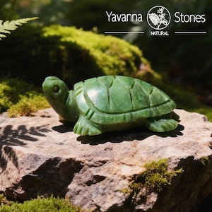 May include: A carved green stone turtle figurine. The turtle is detailed with carved shell segments and flipper-like feet. The figurine is displayed on a natural stone surface, with the text "Yavanna Stones NATURAL" in the background.