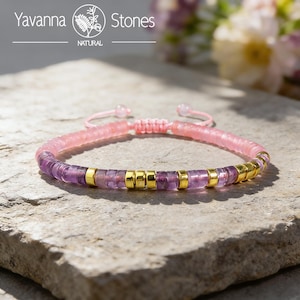 Può includere: Un braccialetto di perline rosa e viola con dettagli dorati. Il braccialetto presenta una combinazione di perline rosa e color ametista, intervallate da perline cilindriche dorate. Il braccialetto è regolabile con un cordoncino rosa e ha il testo "Yavanna Stones".