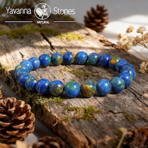 May include: A blue and green beaded bracelet made of natural stones. The bracelet is displayed on a rustic wooden surface with moss and pinecones. The Yavanna Stones logo is visible in the top left corner.