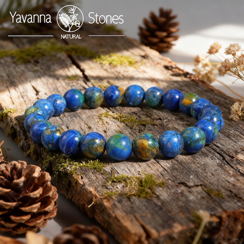 May include: A blue and green beaded bracelet made of natural stones. The bracelet is displayed on a rustic wooden surface with moss and pinecones. The Yavanna Stones logo is visible in the top left corner.