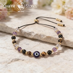 May include: A beaded bracelet featuring a variety of gemstones, including amethyst, tiger's eye, and clear quartz. The bracelet has a black adjustable cord and a gold-colored bead. An evil eye bead is incorporated into the design. The brand name "Yavanna Stones" is visible.
