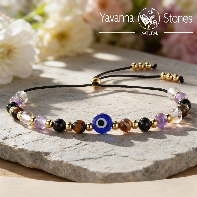 May include: Adjustable bracelet featuring a blue evil eye bead, interspersed with gold-colored beads and various natural stone beads in shades of purple, brown, black, and clear. The bracelet is strung on a black cord.
