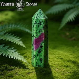 Puede incluir: Una torre de cristal de zoisita verde y rosa se alza sobre musgo verde. El cristal es verde con motas negras y una sección rosa. La parte superior del cristal es puntiaguda. El texto "Yavanna Stones NATURAL" está en la parte superior izquierda.
