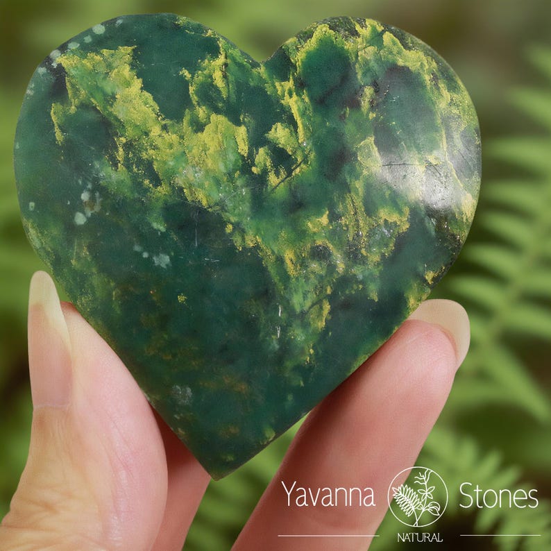 May include: A heart-shaped stone with a green base color and yellow veining. The stone is held in a hand, with the Yavanna Stones logo visible in the bottom right corner. The stone has a natural, organic appearance.