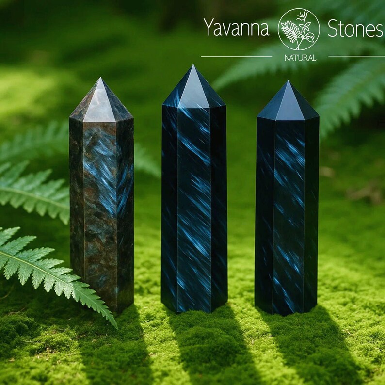 May include: Three natural, polished crystal obelisks with pointed tops. The obelisks are dark blue and brown with streaks of lighter blue. The crystals are displayed on a bed of green moss. The text "Yavanna Stones NATURAL" is at the top.