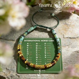 May include: A beaded bracelet with turquoise and gold-colored beads, and a section of brown beads. The bracelet is displayed with a green card that has the text "INTERNATIONAL MORSE CODE" and the Yavanna Stones logo.
