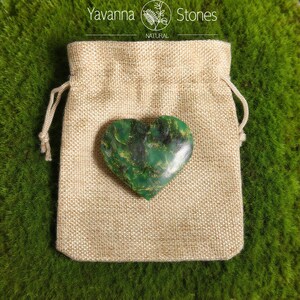 May include: A heart-shaped green stone with dark green and gold veining rests on a beige burlap bag. The bag is closed with a drawstring. The words "Yavanna Stones NATURAL" are printed at the top.