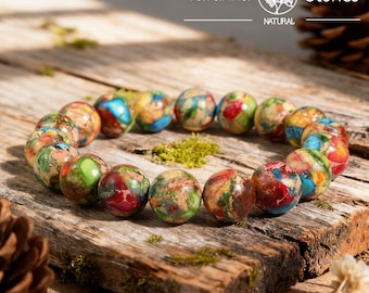 Pode incluir: Uma pulseira feita de pedras naturais redondas e coloridas. As pedras são uma mistura de vermelho, verde, azul e amarelo, dispostas em um padrão circular. A pulseira é exibida em uma superfície de madeira rústica. O texto "Yavanna Stones NATURAL" é visível.