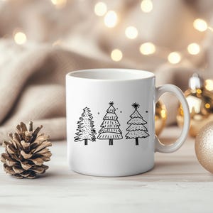 May include: White ceramic mug featuring three black line-drawn Christmas trees. The trees have varying designs, with one featuring a dotted pattern, another with horizontal lines, and the last with a layered look. The mug has a curved handle.