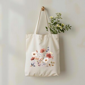 May include: A cream-colored tote bag with a floral design of red, white, and blue flowers. The bag is hanging on a gold hook, and a bouquet of white and yellow flowers is inside the bag.