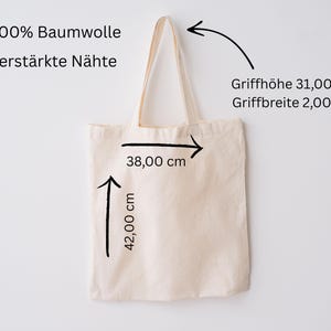 May include: A beige tote bag with cream-colored handles. The bag is 42 cm high and 38 cm wide. The handle height is 31 cm, and the handle width is 2 cm. The text on the bag says "100% Baumwolle" and "verst&auml;rkte N&auml;hte".
