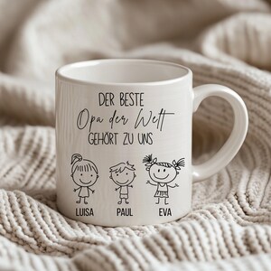 May include: White ceramic mug with a handle, featuring the text "DER BESTE Opa der Welt GEH&Ouml;RT ZU UNS" and three stick figure children with the names Luisa, Paul, and Eva. The mug is on a textured, off-white surface.