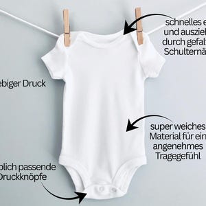May include: A white baby onesie with short sleeves, hanging from a clothesline with a wooden clothespin. The onesie has snap closures at the bottom. Text on the image says "durable print" and "color-matched snaps".