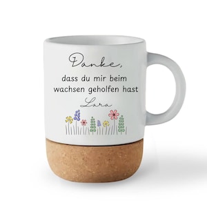 May include: White ceramic mug with a cork base, featuring the text "Danke, dass du mir beim wachsen geholfen hast Lara" and a floral design. The mug has a curved handle and is set against a white background.