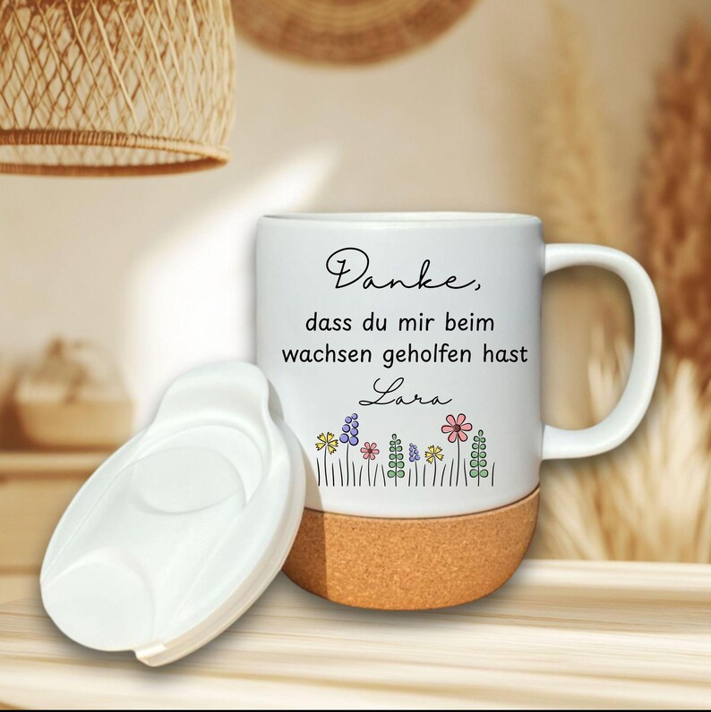 May include: White ceramic mug with a cork base and a white lid. The mug features the text "Danke, dass du mir beim wachsen geholfen hast Lara" and a floral design in various colors. The mug has a handle.