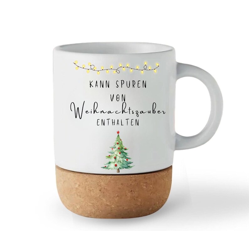 May include: White ceramic mug with a cork base, featuring a Christmas tree illustration and the text "Kann Spuren von Weihnachtszauber enthalten". The mug has a curved handle and a string of yellow lights.