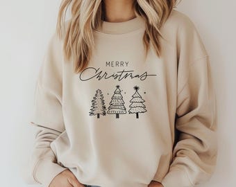 May include: A beige sweatshirt with the words "Merry Christmas" in a script font above three black line-drawn Christmas trees. The sweatshirt has a crew neck and long sleeves.