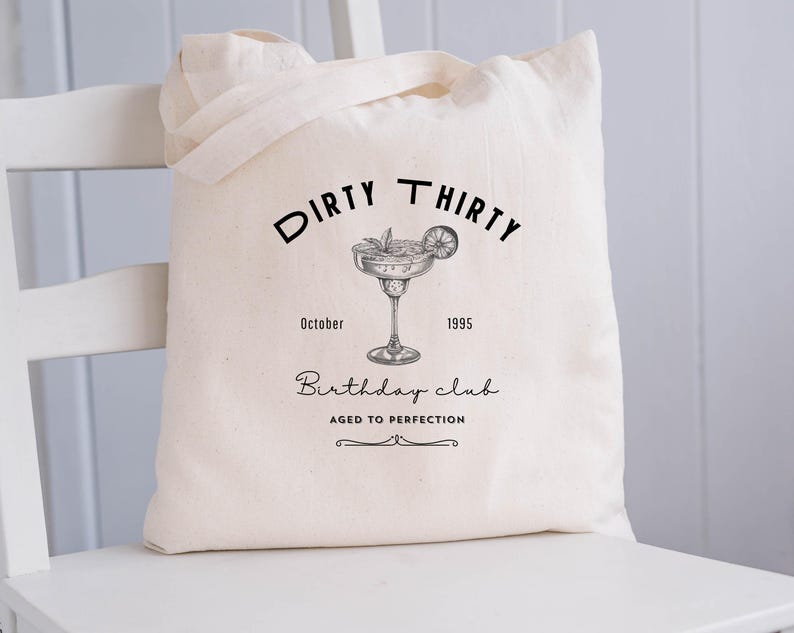 May include: Cream-colored tote bag with black text and a cocktail illustration. The text reads "DIRTY THIRTY Birthday club AGED TO PERFECTION" with the year 1995 and the month October. The bag has two handles.