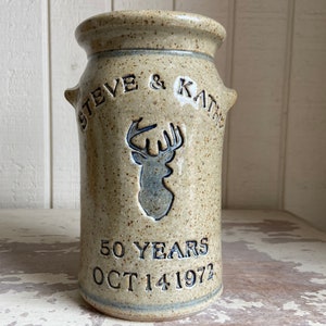 May include: A beige ceramic vase with a deer silhouette and the text "STEVE & KATHY 50 YEARS OCT 14 1972".