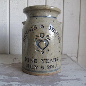 May include: A ceramic jar with a speckled glaze and a heart design. It is inscribed with the names "Dennis & Jennie" and the text "Nine Years July 5, 2011".