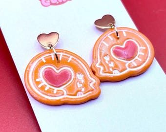 Könnte beinhalten: Orange-weiße Tonohrringe mit Herzdesign. Die Ohrringe haben einen goldfarbenen herzförmigen Stecker und einen passenden orange-weißen Anhänger. Die Ohrringe befinden sich auf einer weißen Karte mit dem Text "JOLLY CUTE CLAY" in Rosa.