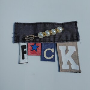 May include: A denim patch with a pearl and gold brooch, and individual fabric letters spelling out the word "F*CK". The letters are in white, red, blue, and tan.