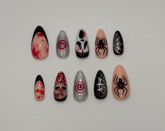 May include: A set of ten artificial nails in various designs. The nails feature a mix of colors, including red, black, silver, and nude. Designs include a spider, spiderweb, and abstract patterns. The nails are almond-shaped.