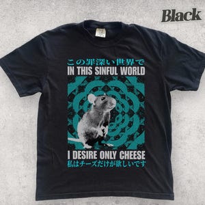 Op de afbeelding: Zwart T-shirt met een afbeelding van een rat en de tekst "IN THIS SINFUL WORLD I DESIRE ONLY CHEESE" in het Engels en Japans. Het ontwerp bevat een turquoise en zwart cirkelvormig patroon.