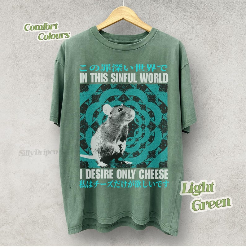 Op de afbeelding: Lichtgroen T-shirt met een rattenafbeelding en de tekst "IN THIS SINFUL WORLD" en "I DESIRE ONLY CHEESE". Het ontwerp heeft een turquoise en zwarte mandala-stijl achtergrond. Het shirt is een comfort kleur.