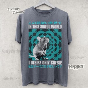Op de afbeelding: Een grijs t-shirt met een afbeelding van een rat en de tekst "IN THIS SINFUL WORLD" en "I DESIRE ONLY CHEESE". Het ontwerp bevat een turquoise en wit cirkelvormig patroon. Het shirt is gelabeld met "Comfort Colours" en "Pepper".