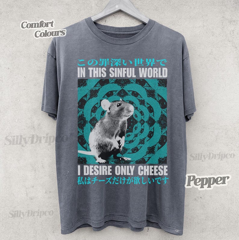Op de afbeelding: Een grijs t-shirt met een afbeelding van een rat en de tekst "IN THIS SINFUL WORLD" en "I DESIRE ONLY CHEESE". Het ontwerp bevat een turquoise en wit cirkelvormig patroon. Het shirt is gelabeld met "Comfort Colours" en "Pepper".
