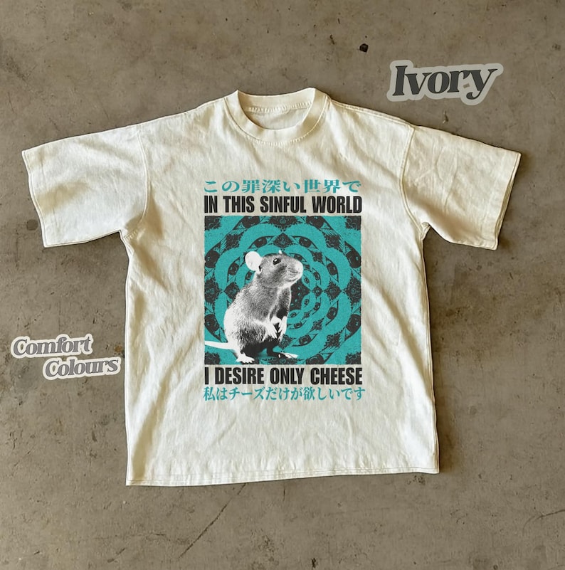 Op de afbeelding: Ivoor t-shirt met een rattenafbeelding en de tekst "IN THIS SINFUL WORLD" en "I DESIRE ONLY CHEESE". Het shirt is gemarkeerd met "Comfort Colours".
