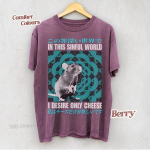 Op de afbeelding: Bessenkleurig T-shirt met een rattenafbeelding en de tekst "IN THIS SINFUL WORLD" erboven. Daaronder staat "I DESIRE ONLY CHEESE". Het shirt hangt aan een houten hanger.