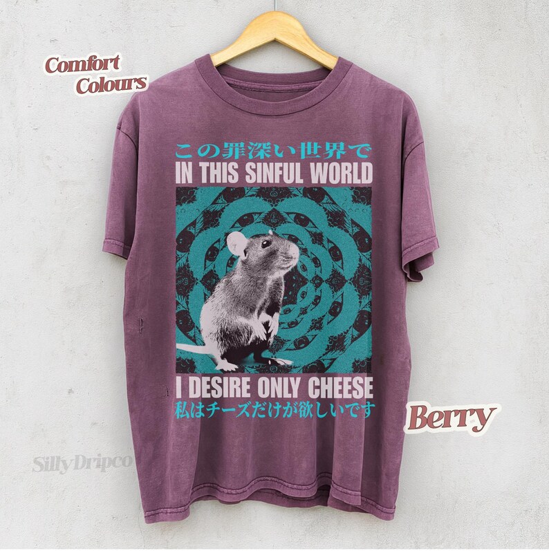 Op de afbeelding: Bessenkleurig T-shirt met een rattenafbeelding en de tekst "IN THIS SINFUL WORLD" erboven. Daaronder staat "I DESIRE ONLY CHEESE". Het shirt hangt aan een houten hanger.