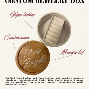 May include: A round jewellery box featuring a bamboo lid with the white script text Mrs Boyd and small pearl accents. The interior is lined with white vegan leather and includes a dedicated section with six padded slots for rings or small items.