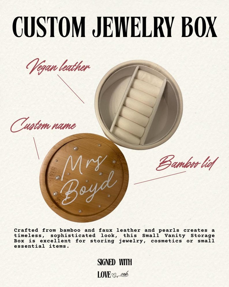 May include: A round jewellery box featuring a bamboo lid with the white script text Mrs Boyd and small pearl accents. The interior is lined with white vegan leather and includes a dedicated section with six padded slots for rings or small items.