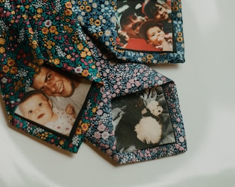 May include: Two neckties featuring a dark blue fabric with a dense floral pattern in shades of yellow, pink, and light blue. Each tie has a rectangular photograph printed on the back lining, showing portraits of people and a small dog.