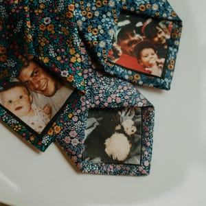 May include: Three floral patterned neckties with family photos printed on the inside. The ties have a navy blue background with a pattern of small flowers in shades of yellow, pink, and white. The photos show a baby, a family, and a dog.