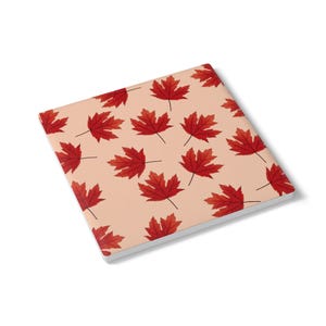May include: A square coaster with a light peach background featuring a repeating pattern of vibrant red maple leaves. The coaster has a clean white edge and a flat surface, displaying multiple leaves oriented in various directions across the top.