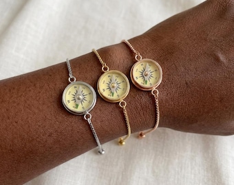 May include: Three adjustable chain bracelets featuring circular compass charms. One bracelet is silver-toned, one is gold-toned, and one is rose gold-toned. Each compass face has a cream background with black directional markings and a central needle.