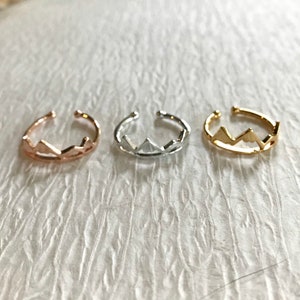 May include: Three mountain-shaped rings in rose gold, silver, and gold.