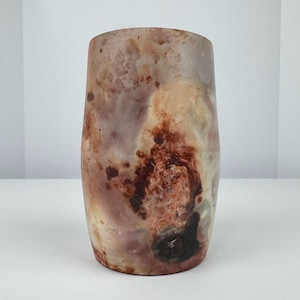 May include: A cylindrical vase with a unique, marbled appearance. The vase features a blend of colors, including shades of brown, red, and cream, creating a natural, organic aesthetic. The vase is a decorative item, suitable for displaying flowers or as a standalone art piece.